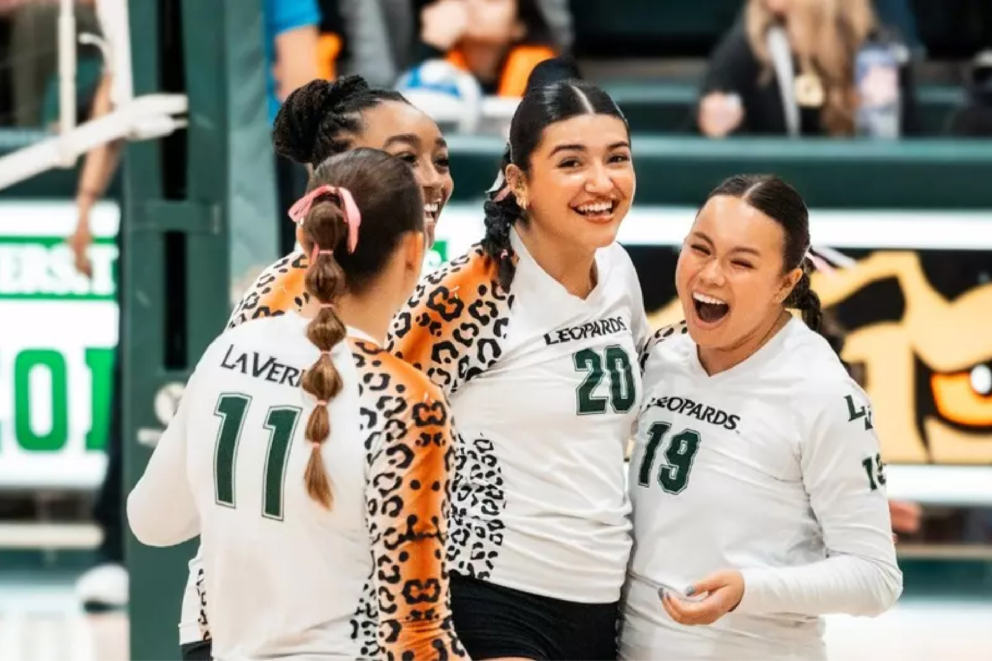 Women's volleyball players standing together and cheering.